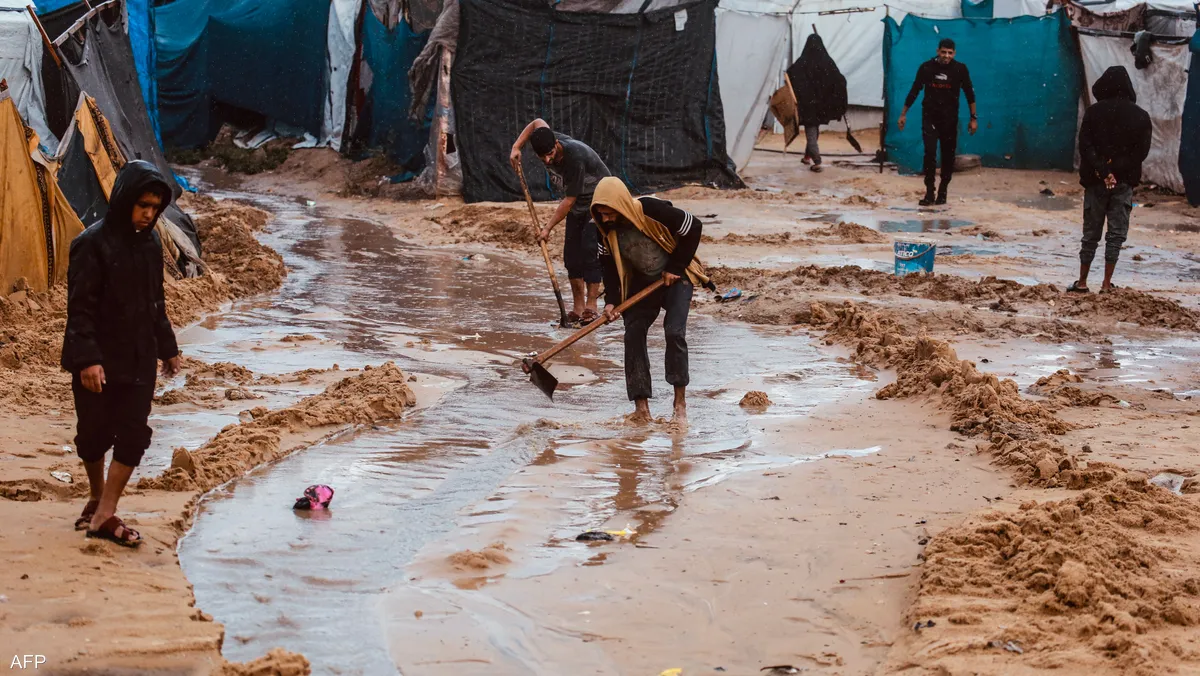 سيول تجتاح مخيمًا للنازحين في غزة، تظهر فيها خيام ممزقة وأطفال يقفون وسط مياه بنية غزيرة